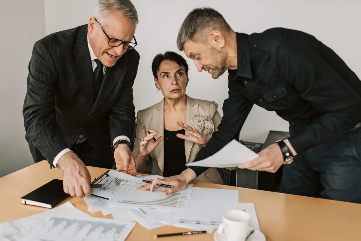 Three colleagues leaning over printed documents during a focused planning discussion