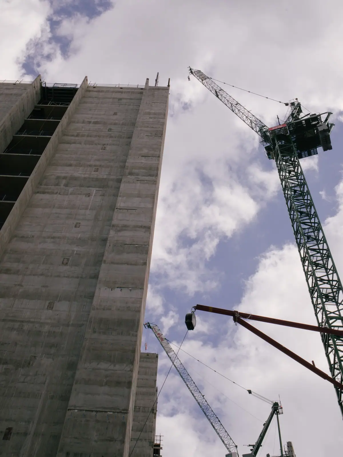 Tower crane beside a concrete building under construction against a cloudy sky