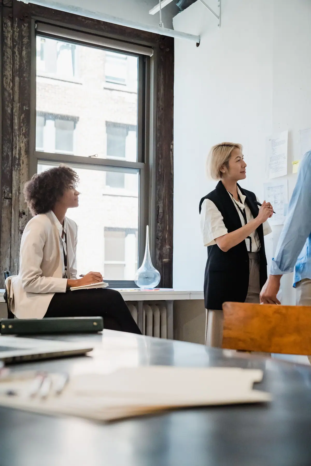 Two colleagues talking through a project beside a large office window