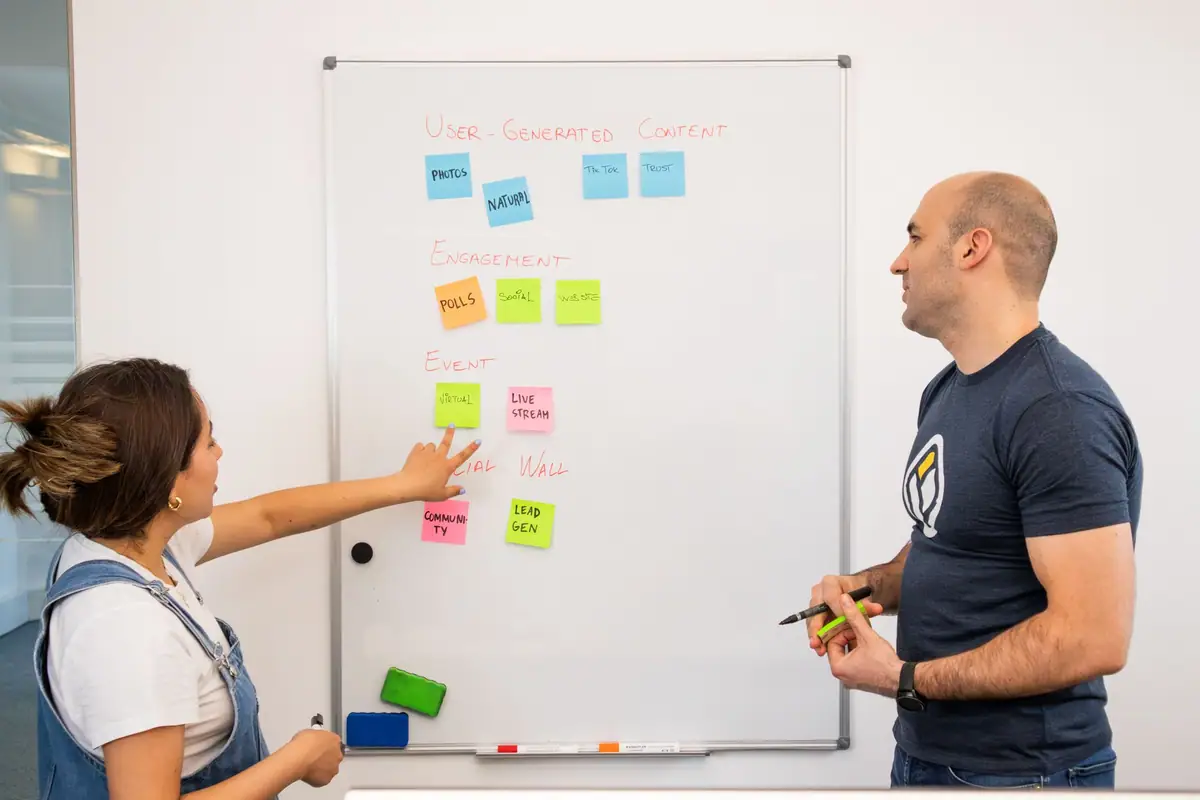 Two colleagues organizing sticky notes on a whiteboard while mapping a process
